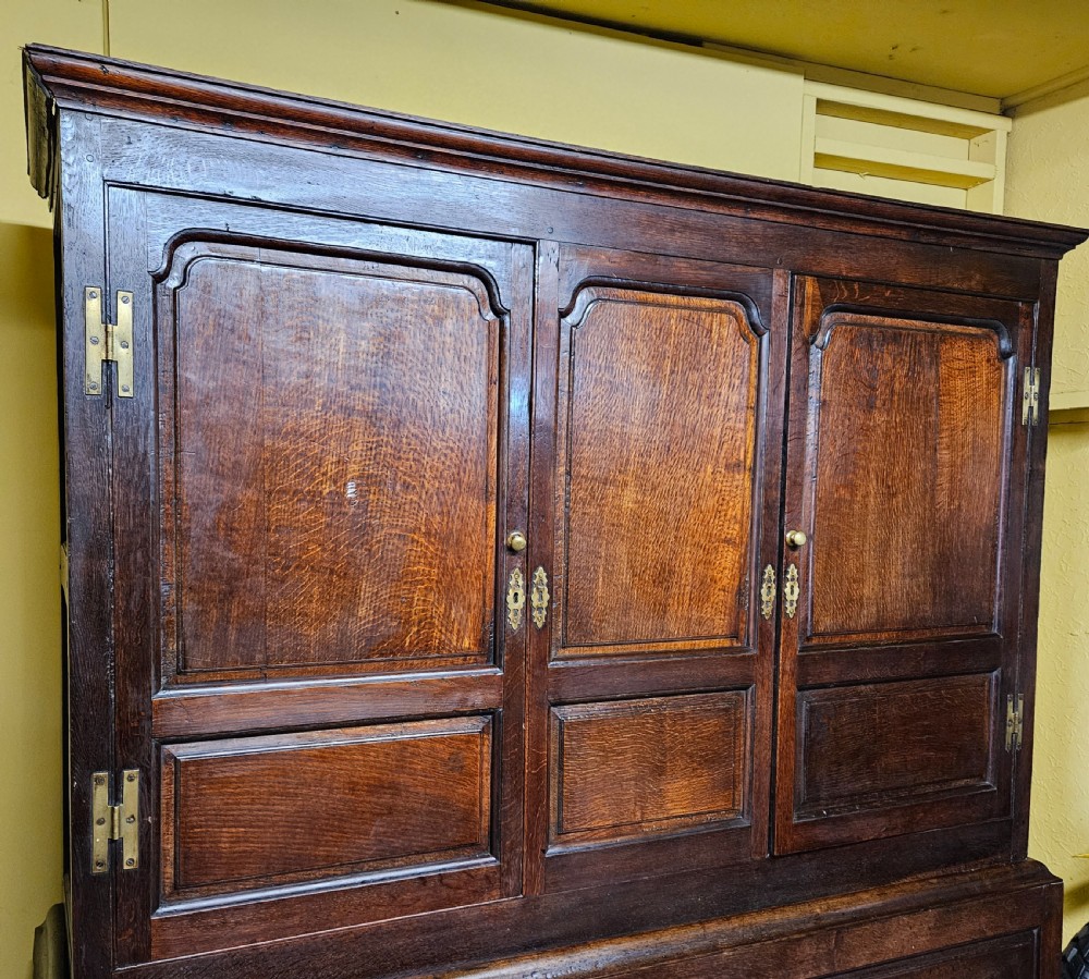 A large period dark oak livery cupboard featuring fielded arch-topped panel doors above a lower section fitted with drawers and brass hardware. View XI