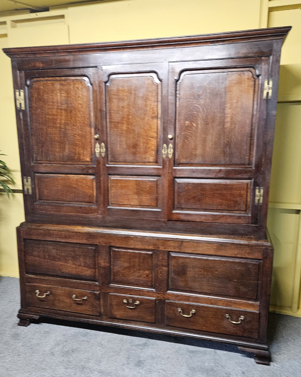 A large period dark oak livery cupboard featuring fielded arch-topped panel doors above a lower section fitted with drawers and brass hardware. View XV