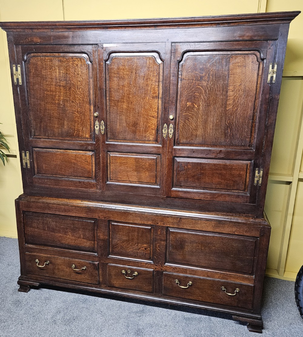 A large period dark oak livery cupboard featuring fielded arch-topped panel doors above a lower section fitted with drawers and brass hardware. View XVI