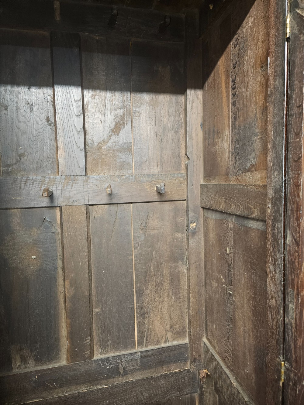 A large period dark oak livery cupboard featuring fielded arch-topped panel doors above a lower section fitted with drawers and brass hardware. View XXII