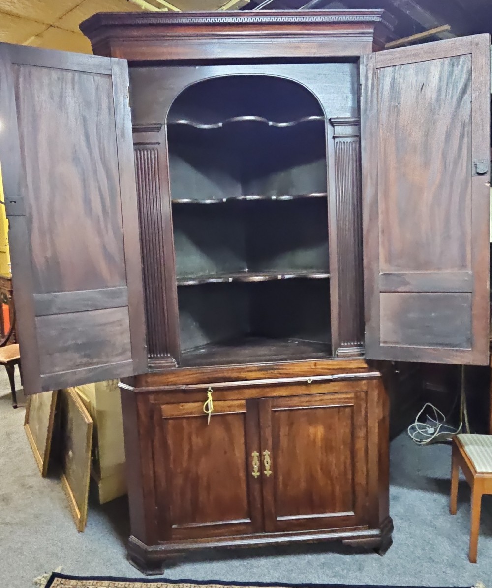 A tall two-tier Georgian mahogany corner cabinet with open upper panelled doors revealing arched interior shelving, set above a two-door base cabinet.