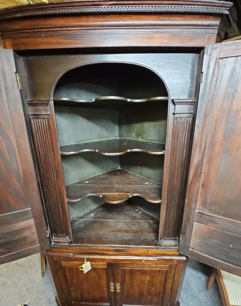A tall two-tier Georgian mahogany corner cabinet with open upper panelled doors revealing arched interior shelving, set above a two-door base cabinet. View VI