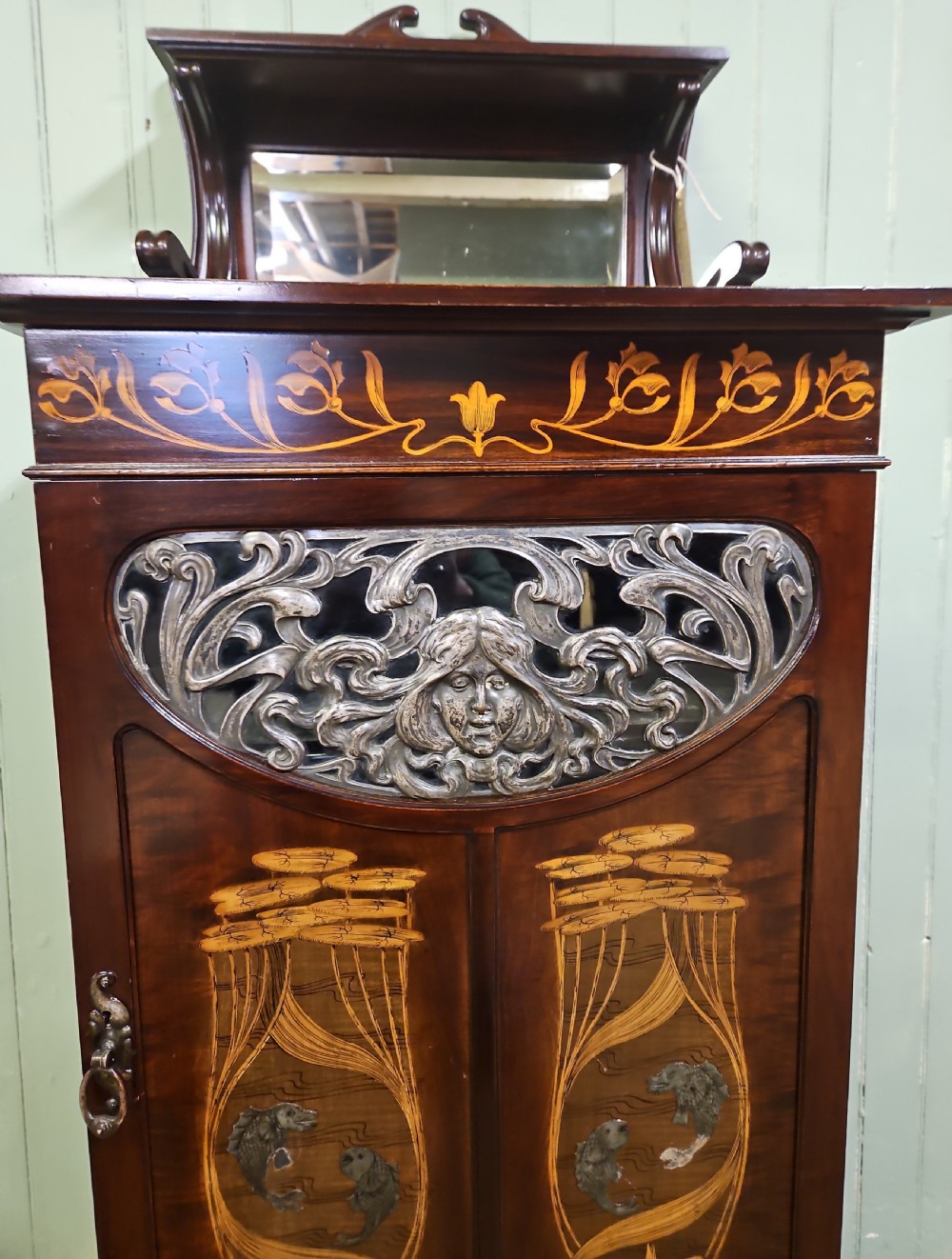 An Art Nouveau dark mahogany music cabinet featuring detailed wood marquetry, a pierced metal cartouche panel, and an upper mirrored gallery shelf. View V