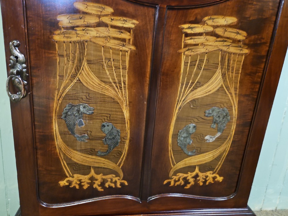 An Art Nouveau dark mahogany music cabinet featuring detailed wood marquetry, a pierced metal cartouche panel, and an upper mirrored gallery shelf. View XIV