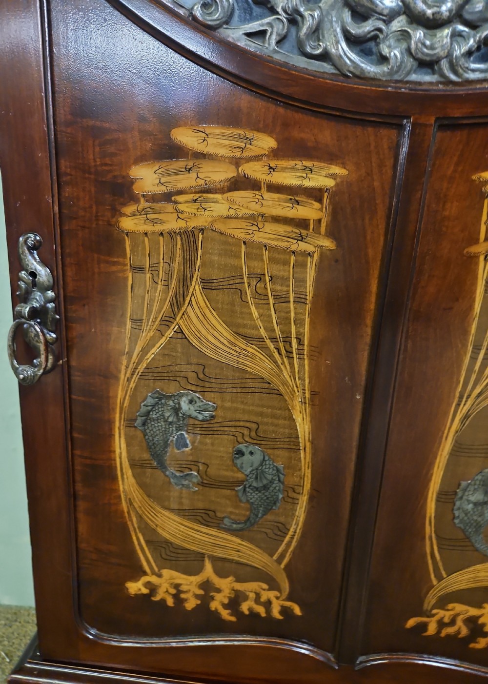 An Art Nouveau dark mahogany music cabinet featuring detailed wood marquetry, a pierced metal cartouche panel, and an upper mirrored gallery shelf. View XVI