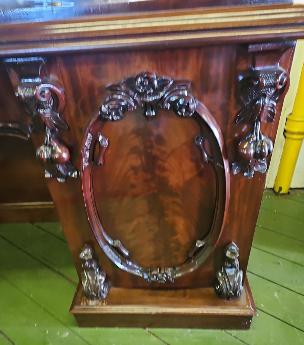 A Victorian mahogany sideboard with a large carved scrollwork framed mirror top, a serpentine surface, and twin pedestal cupboards with oval mouldings. View II