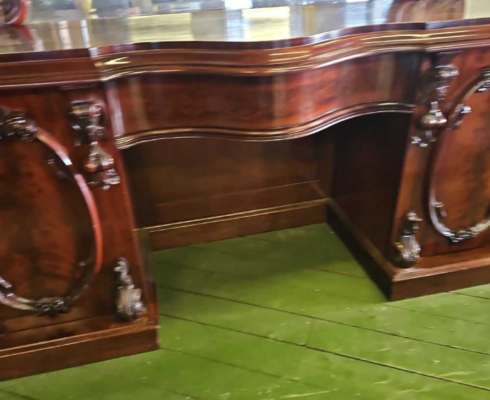 A Victorian mahogany sideboard with a large carved scrollwork framed mirror top, a serpentine surface, and twin pedestal cupboards with oval mouldings. View III