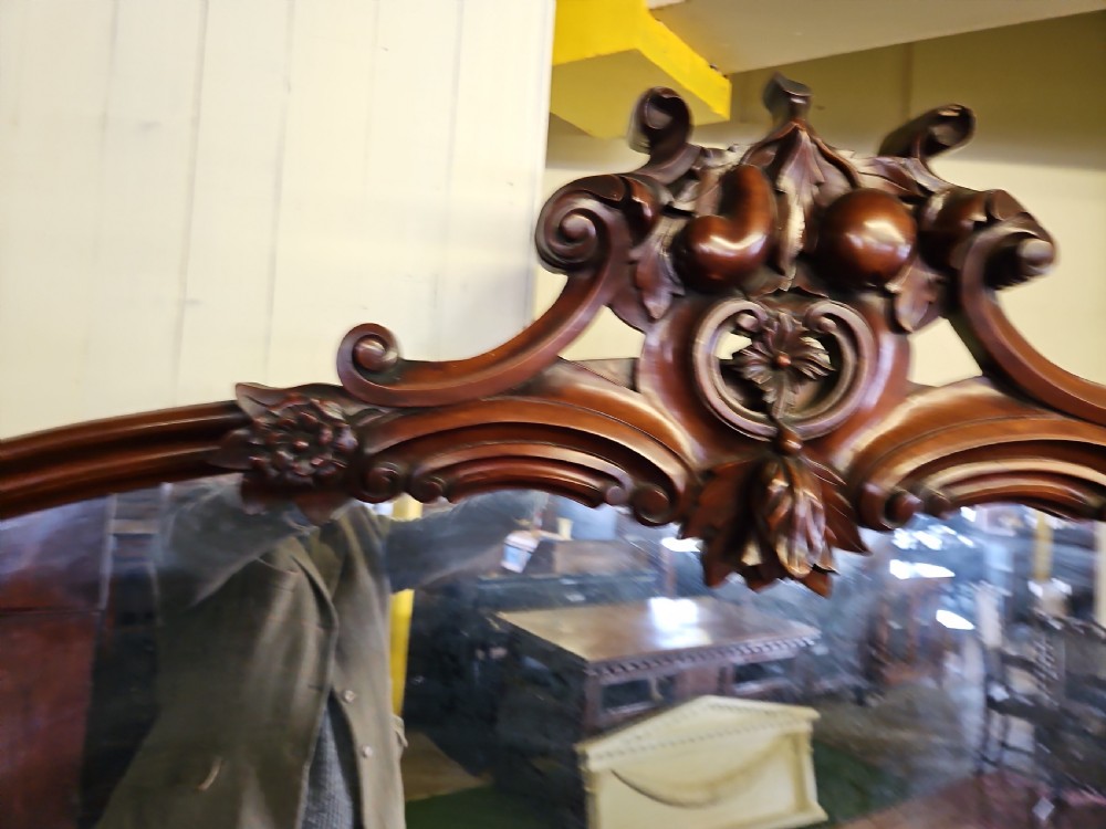 A Victorian mahogany sideboard with a large carved scrollwork framed mirror top, a serpentine surface, and twin pedestal cupboards with oval mouldings. View X