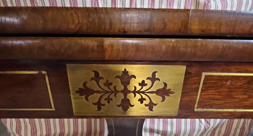 A Regency rosewood games table featuring brass inlay embellishments, a central pedestal, and splayed quadripartite legs with brass caps. View VI
