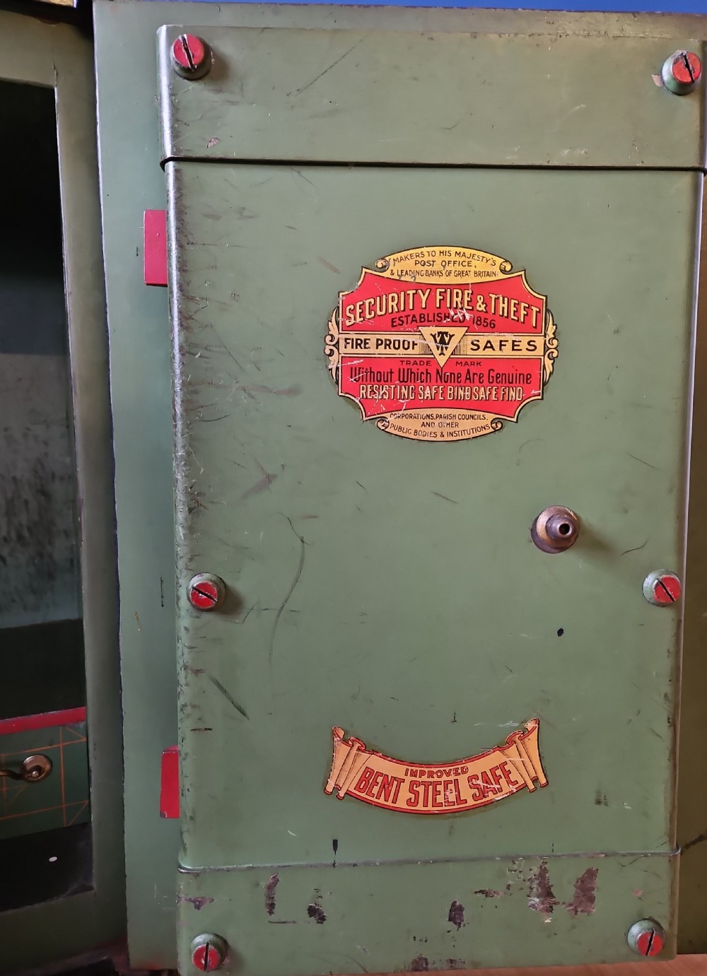 A black Victorian cast iron safe featuring a central brass makers plaque, gold line decoration, a brass T-bar handle, and a key inserted into the lock. View II