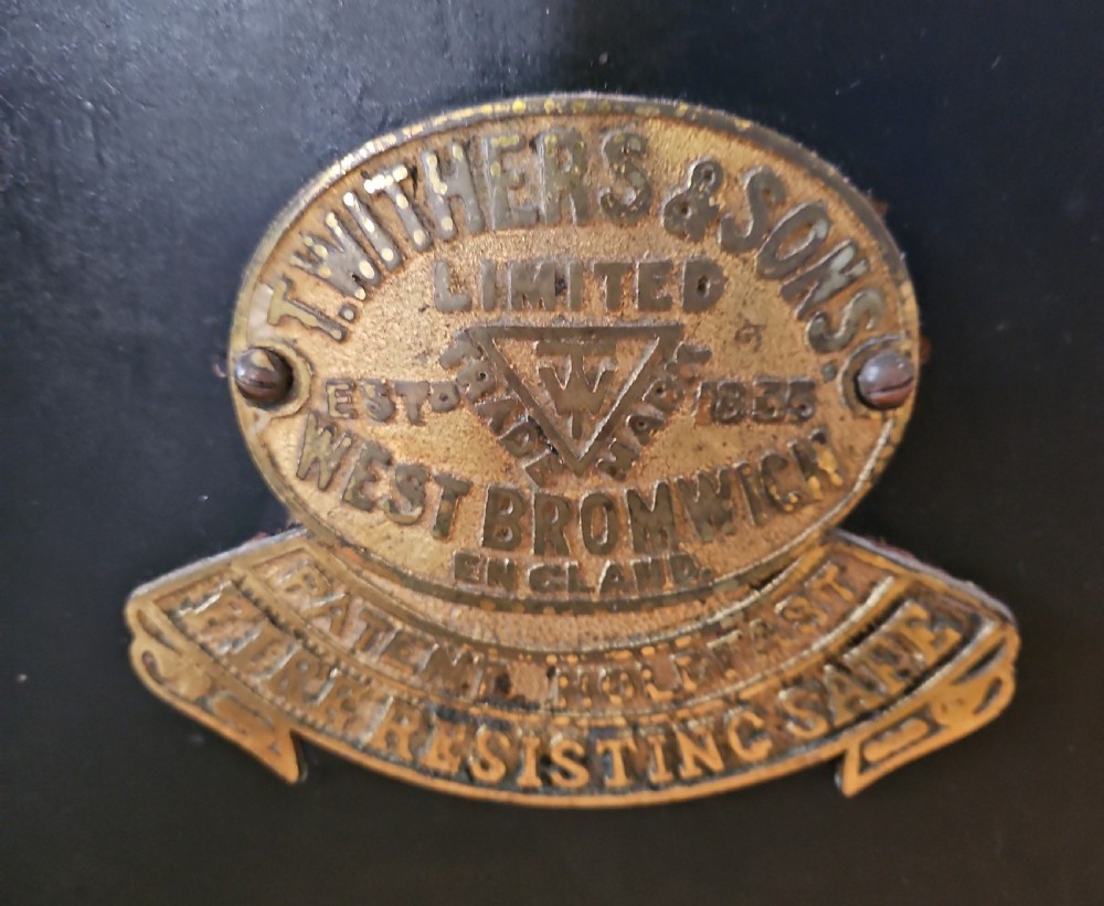 A black Victorian cast iron safe featuring a central brass makers plaque, gold line decoration, a brass T-bar handle, and a key inserted into the lock. View III