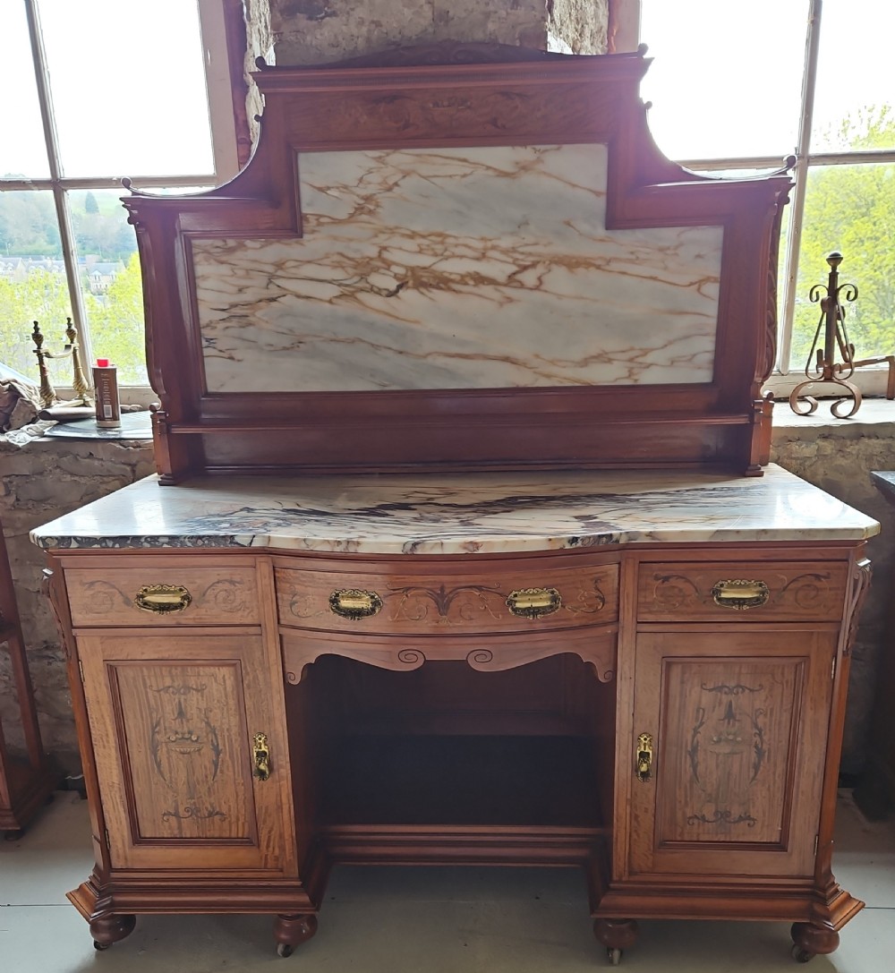 A satinwood inlaid washstand featuring a dark veined marble surface and splashback above three drawers and twin cupboard doors with inlaid urn motifs.