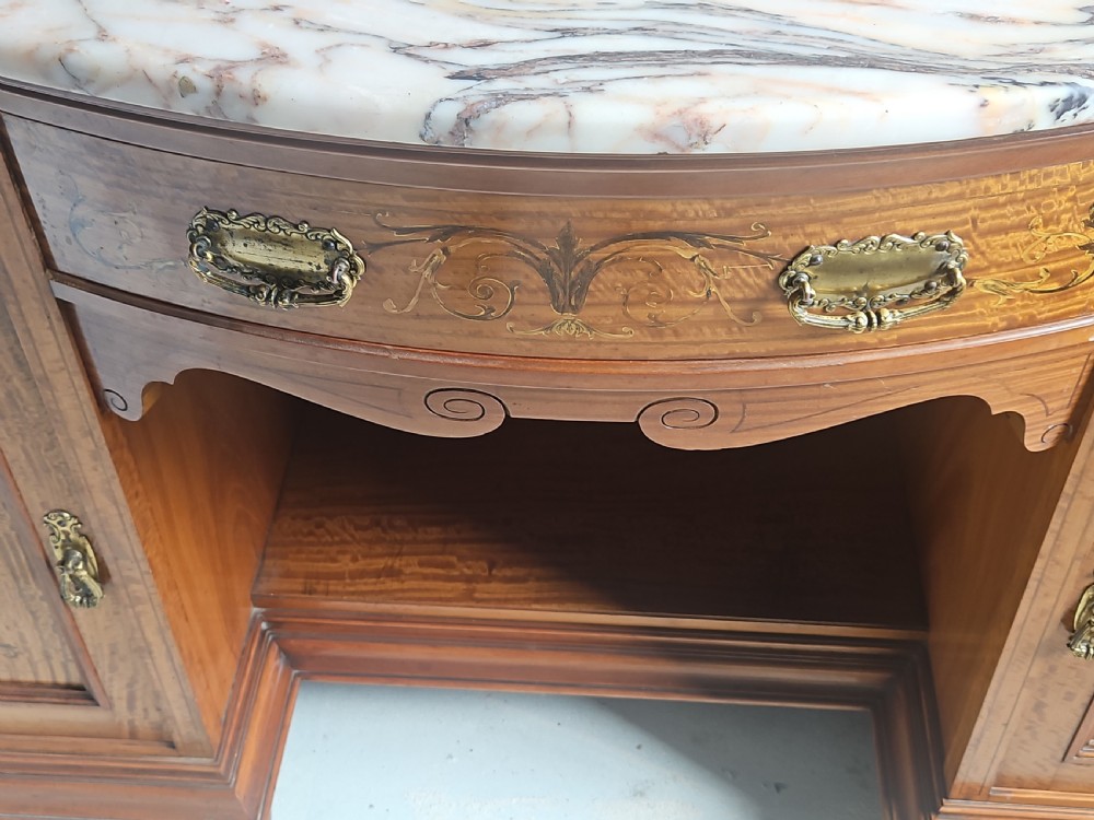 A satinwood inlaid washstand featuring a dark veined marble surface and splashback above three drawers and twin cupboard doors with inlaid urn motifs. View VI