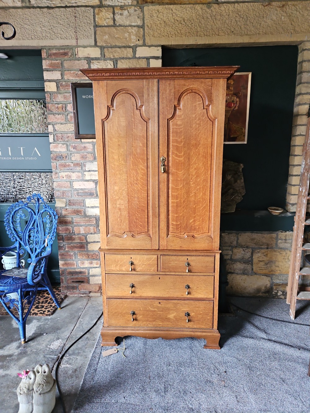 An antique oak linen press featuring an upper two-door cupboard with arched panels above four drawers with brass handles.