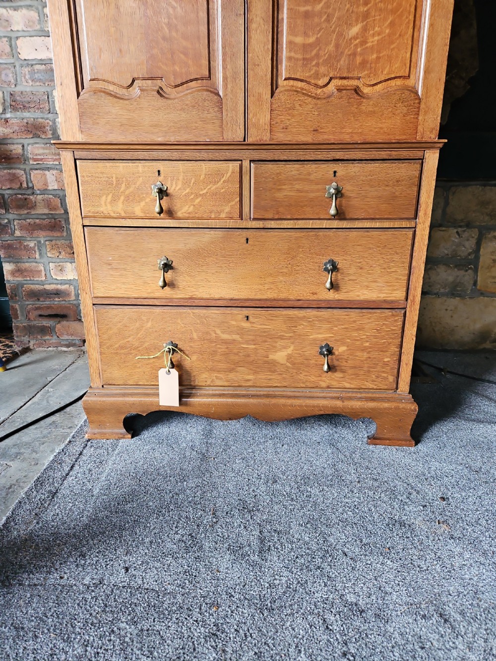 An antique oak linen press featuring an upper two-door cupboard with arched panels above four drawers with brass handles. View II