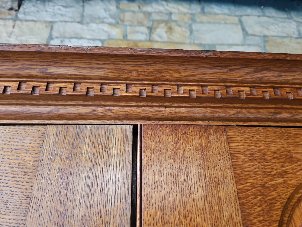 An antique oak linen press featuring an upper two-door cupboard with arched panels above four drawers with brass handles. View IV