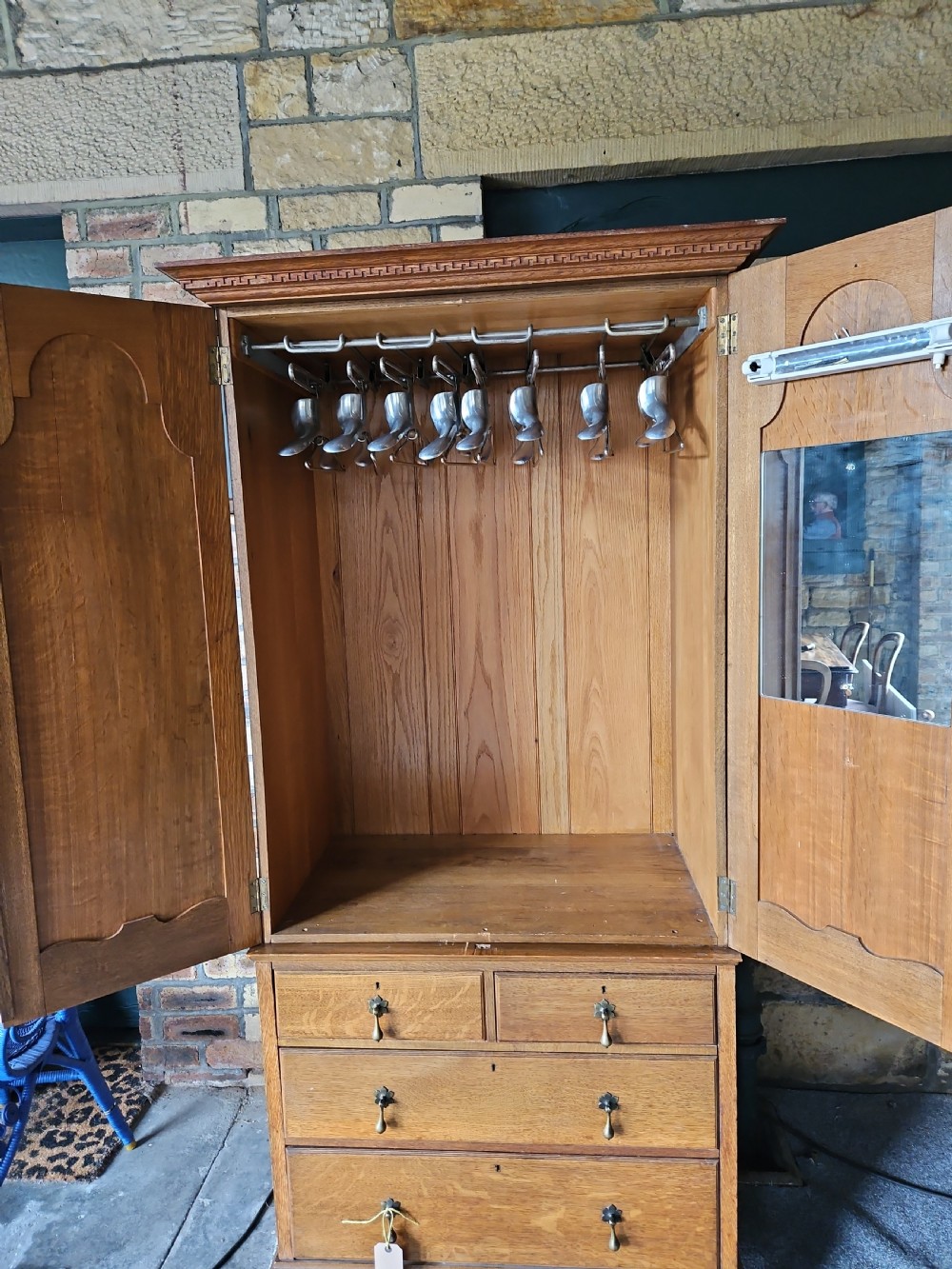 An antique oak linen press featuring an upper two-door cupboard with arched panels above four drawers with brass handles. View V