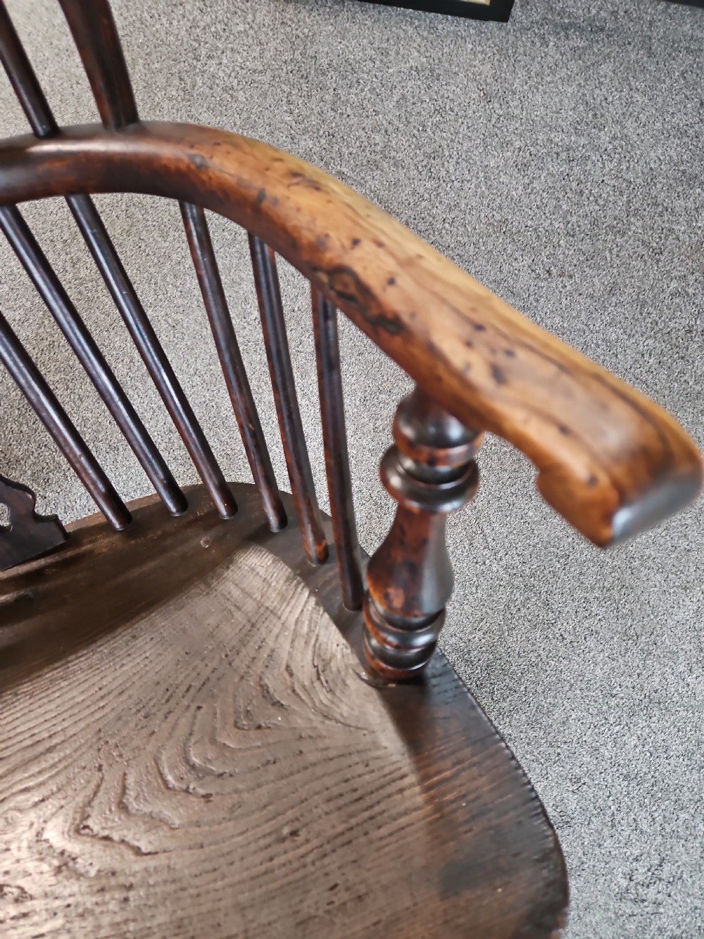 An antique dark yew wood Windsor armchair featuring a curved hoop back, a pierced central splat, turned spindles, and carved wooden arms supported by turned legs. View III