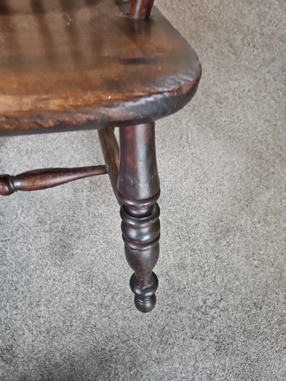 An antique dark yew wood Windsor armchair featuring a curved hoop back, a pierced central splat, turned spindles, and carved wooden arms supported by turned legs. View IV