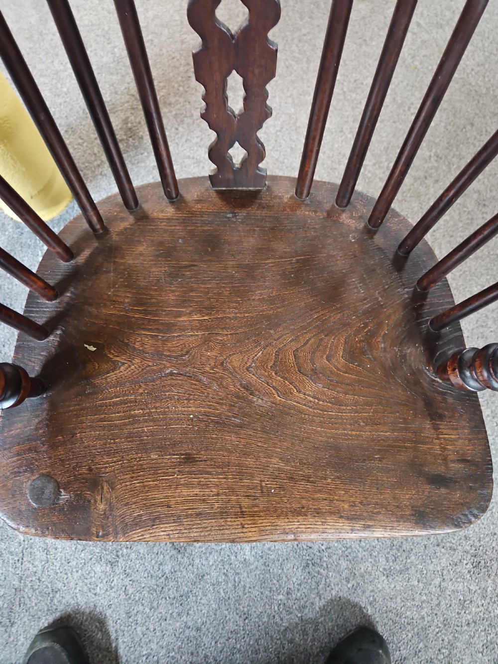 An antique dark yew wood Windsor armchair featuring a curved hoop back, a pierced central splat, turned spindles, and carved wooden arms supported by turned legs. View V