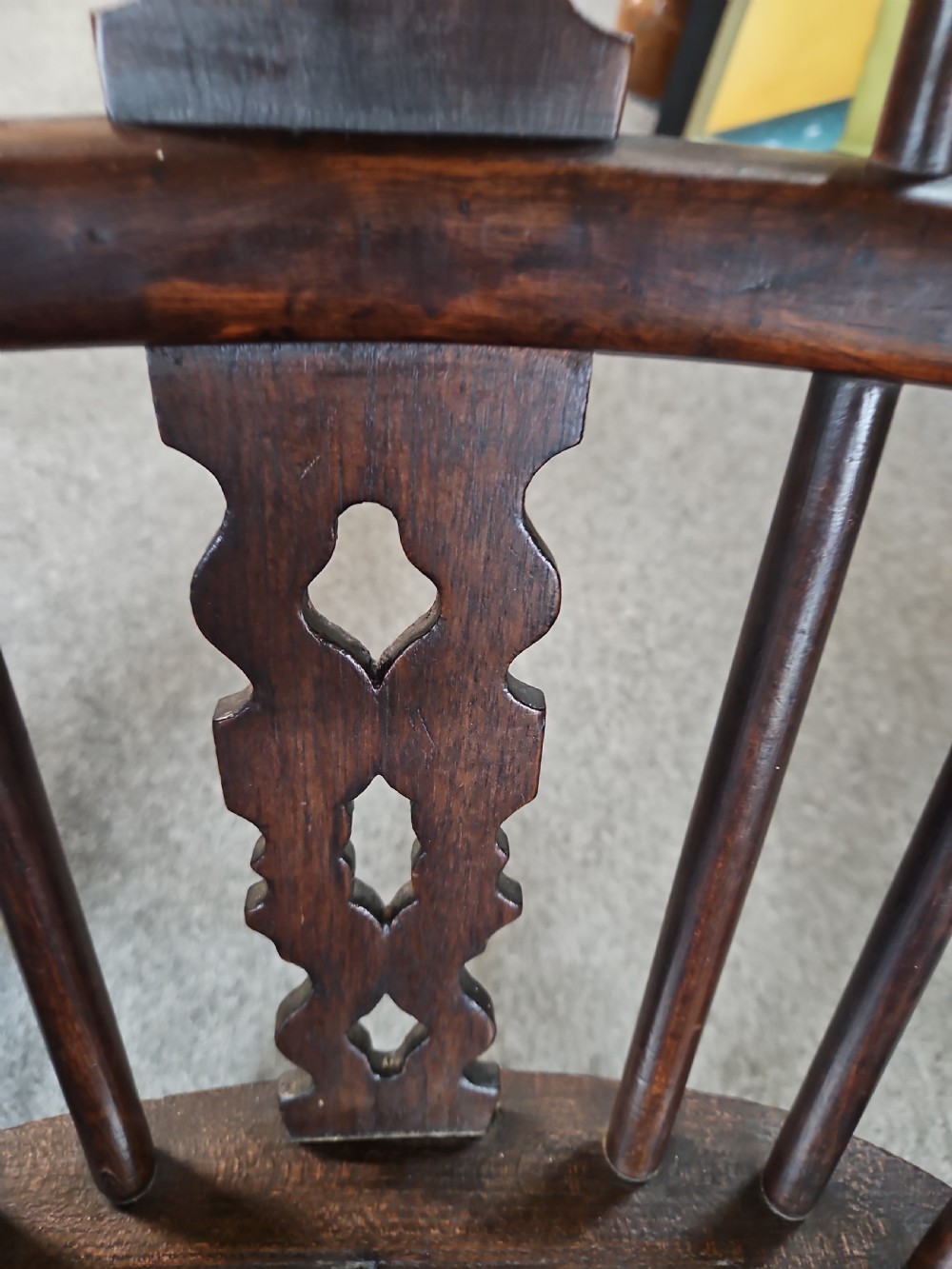 An antique dark yew wood Windsor armchair featuring a curved hoop back, a pierced central splat, turned spindles, and carved wooden arms supported by turned legs. View VI