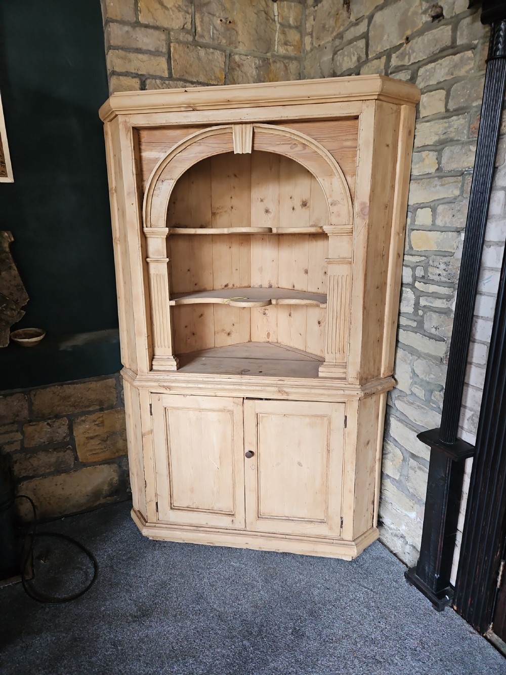 A tall Victorian pine corner cabinet with an arched open display top containing two shelves over a lower panelled double-door cupboard.
