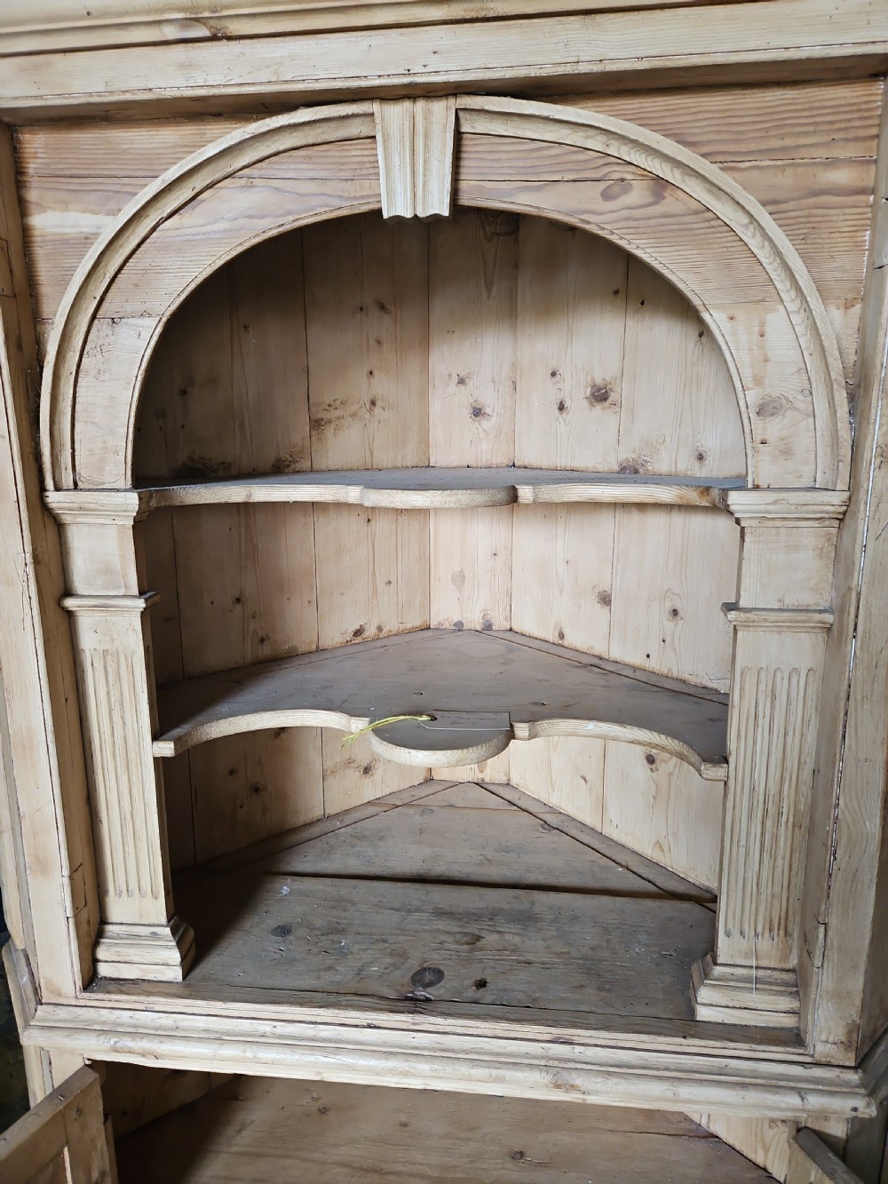 A tall Victorian pine corner cabinet with an arched open display top containing two shelves over a lower panelled double-door cupboard. View IV