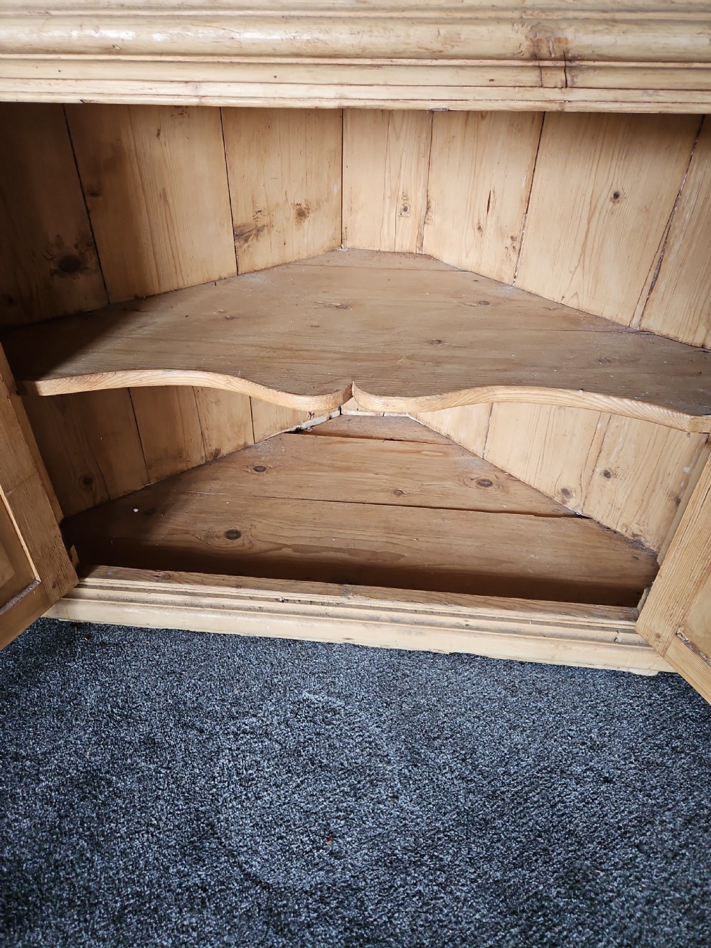 A tall Victorian pine corner cabinet with an arched open display top containing two shelves over a lower panelled double-door cupboard. View V