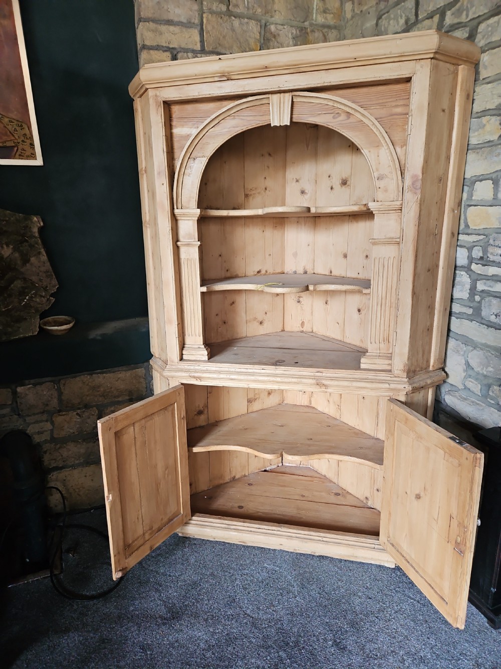 A tall Victorian pine corner cabinet with an arched open display top containing two shelves over a lower panelled double-door cupboard. View VI