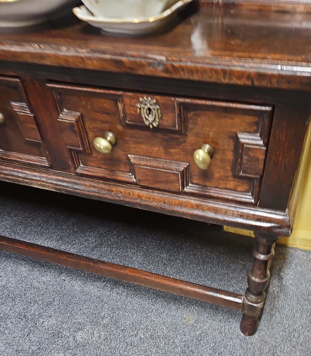 A dark oak Welsh dresser featuring a tall multi-tiered open plate rack top above three drawers with geometric mouldings and turned legs. View III