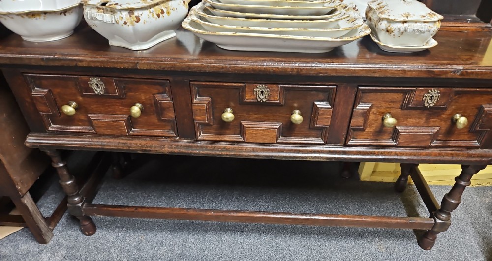 A dark oak Welsh dresser featuring a tall multi-tiered open plate rack top above three drawers with geometric mouldings and turned legs. View VI