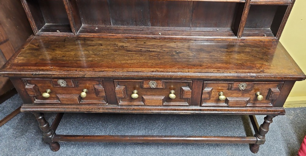 A dark oak Welsh dresser featuring a tall multi-tiered open plate rack top above three drawers with geometric mouldings and turned legs. View VIII