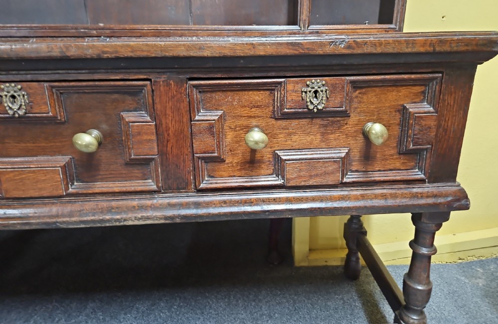 A dark oak Welsh dresser featuring a tall multi-tiered open plate rack top above three drawers with geometric mouldings and turned legs. View IX