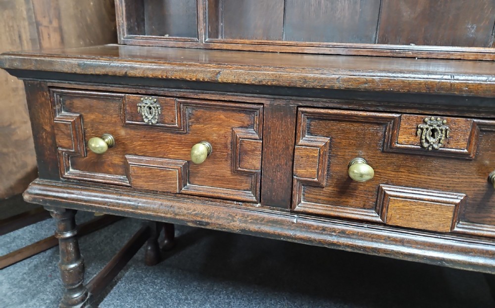 A dark oak Welsh dresser featuring a tall multi-tiered open plate rack top above three drawers with geometric mouldings and turned legs. View X