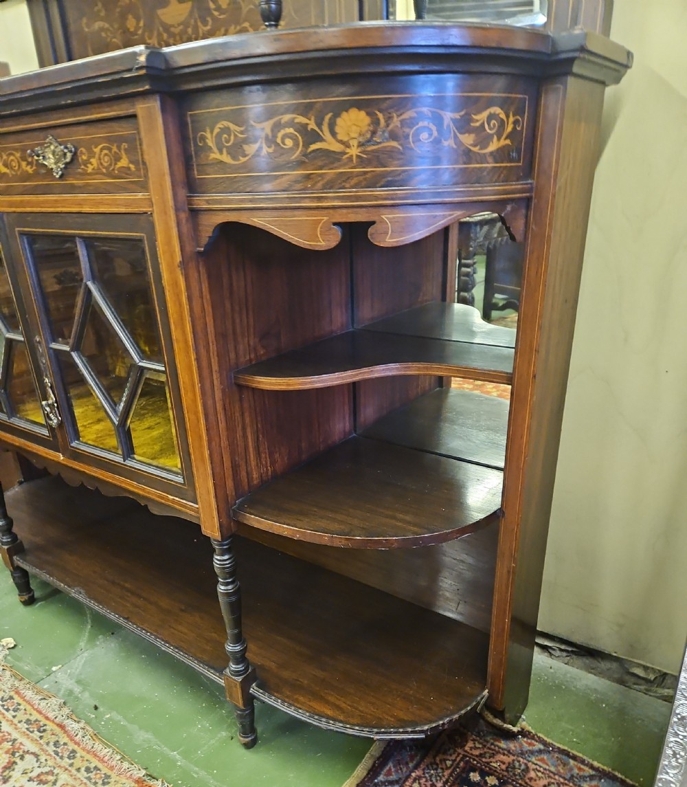An Edwardian rosewood cabinet featuring intricate marquetry inlay, multiple mirrored panels, open tier shelving, and central glass-front doors. View V