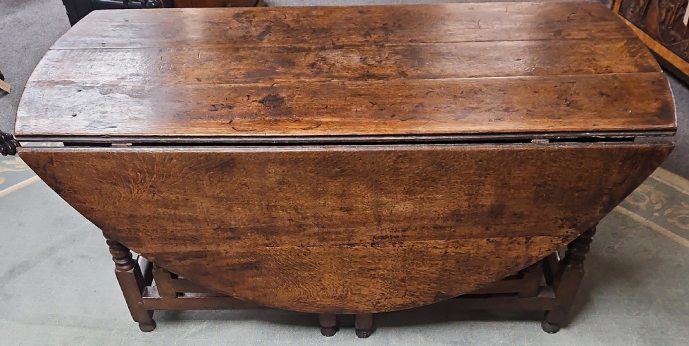 An antique dark oak double gateleg table shown with folded oval side leaves, turned legs, and lower wooden stretchers.