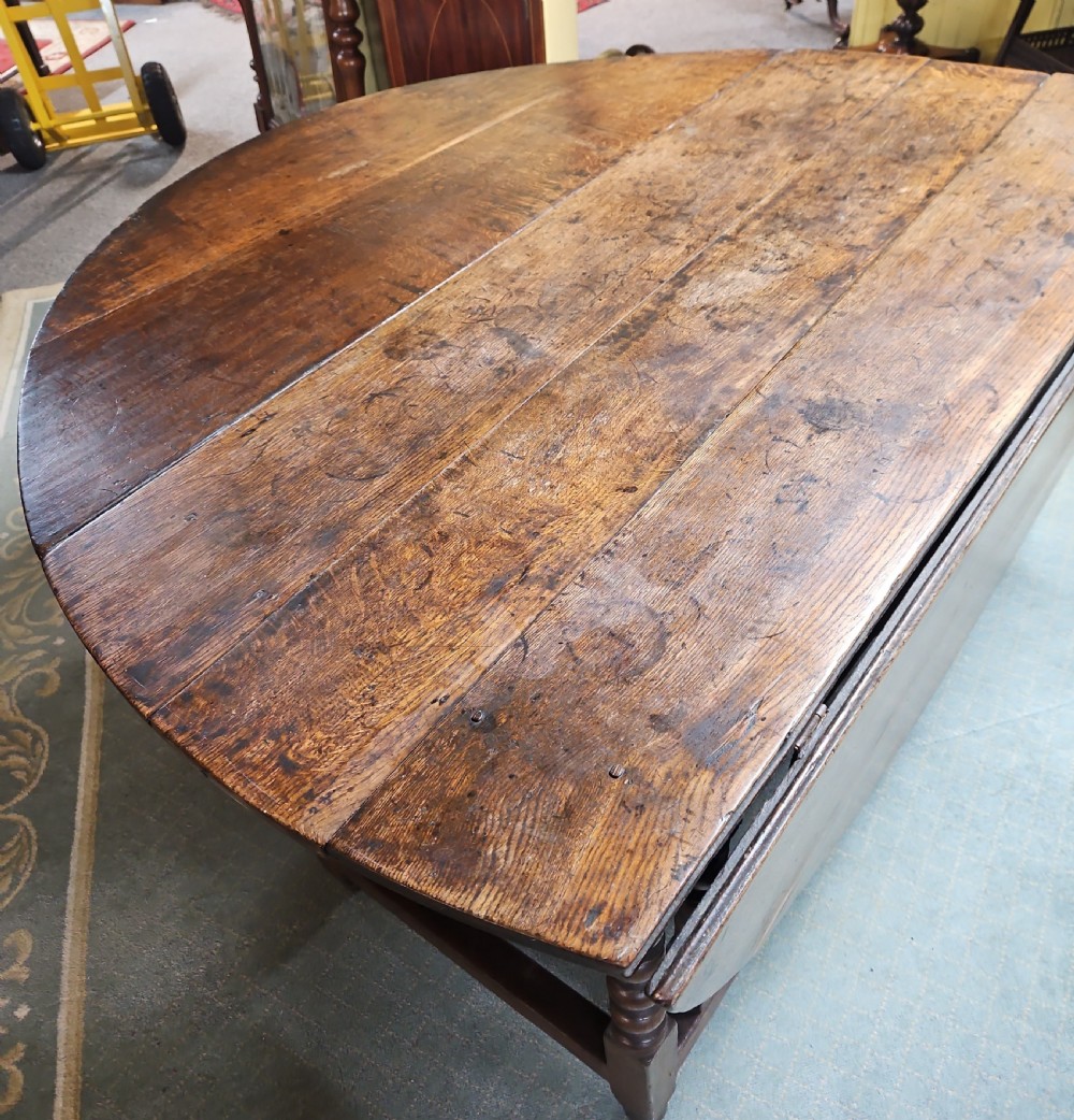 An antique dark oak double gateleg table shown with folded oval side leaves, turned legs, and lower wooden stretchers. View II