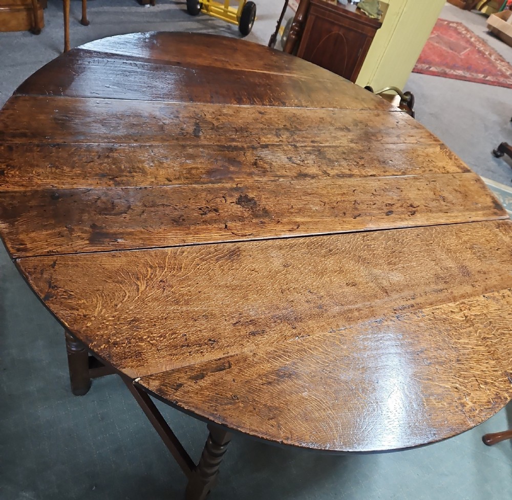 An antique dark oak double gateleg table shown with folded oval side leaves, turned legs, and lower wooden stretchers. View III