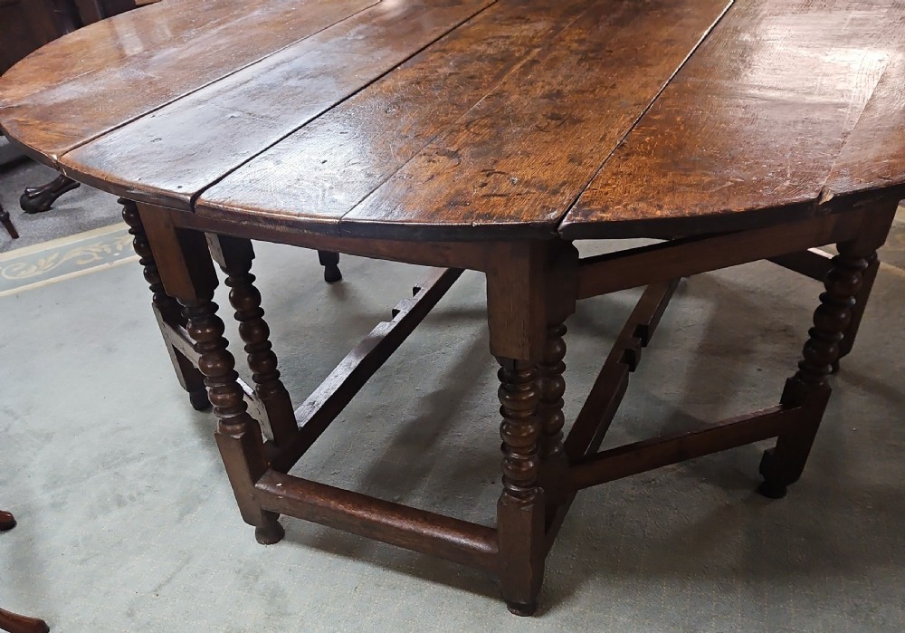 An antique dark oak double gateleg table shown with folded oval side leaves, turned legs, and lower wooden stretchers. View IV