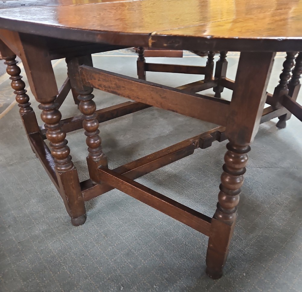 An antique dark oak double gateleg table shown with folded oval side leaves, turned legs, and lower wooden stretchers. View V
