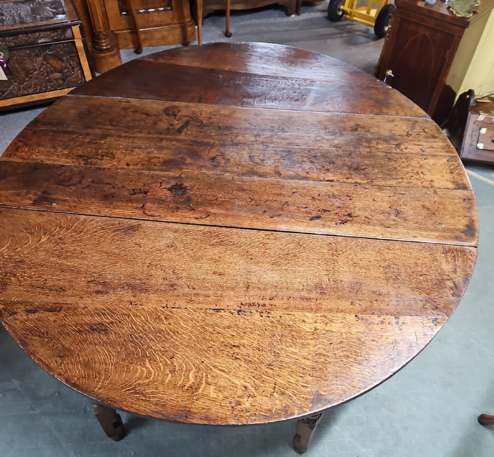 An antique dark oak double gateleg table shown with folded oval side leaves, turned legs, and lower wooden stretchers. View VI