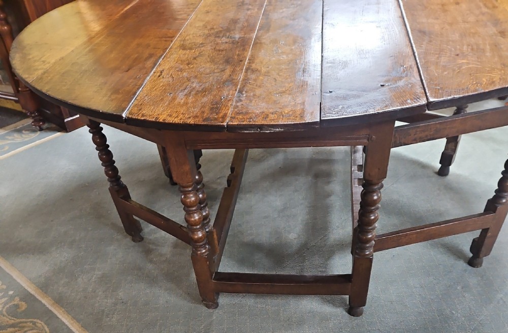 An antique dark oak double gateleg table shown with folded oval side leaves, turned legs, and lower wooden stretchers. View VII