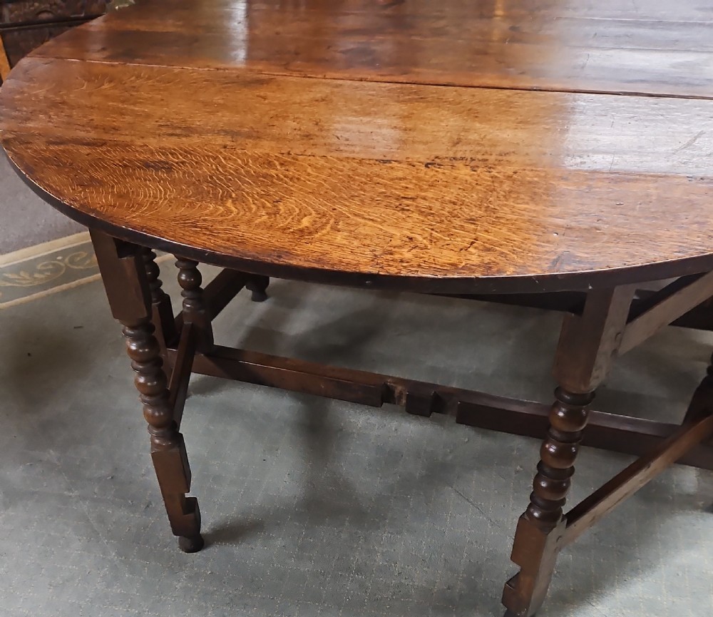 An antique dark oak double gateleg table shown with folded oval side leaves, turned legs, and lower wooden stretchers. View VIII
