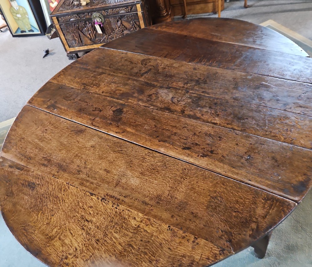 An antique dark oak double gateleg table shown with folded oval side leaves, turned legs, and lower wooden stretchers. View IX