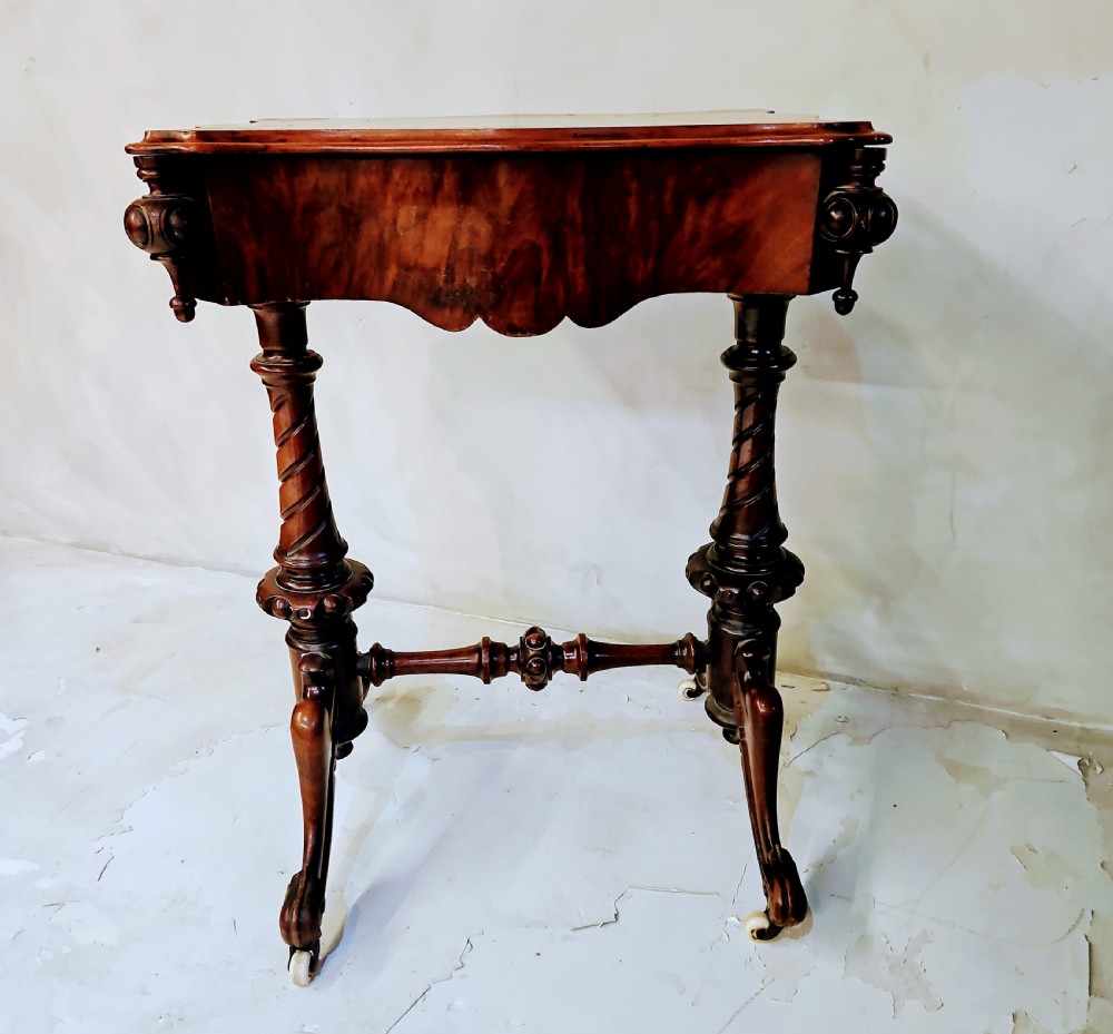 A Victorian walnut work table featuring spiral-turned twin supports, a carved central stretcher, and shaped feet resting on white porcelain castors.