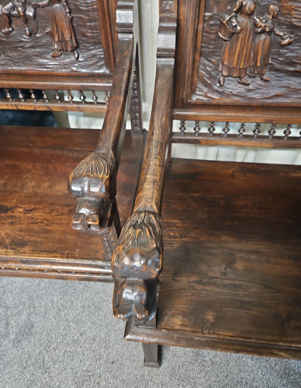 A pair of dark carved oak Breton armchairs featuring backrest panels with relief scenes of folk figures and turned spindle galleries. View III