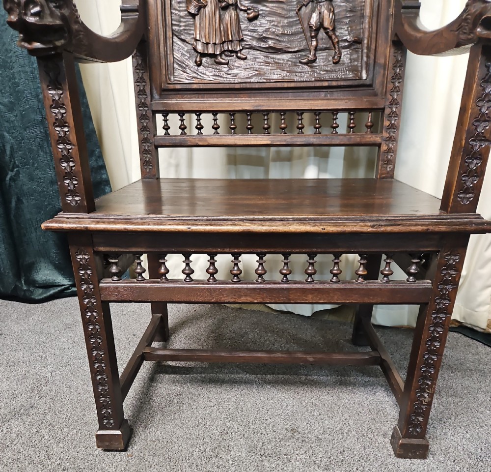 A pair of dark carved oak Breton armchairs featuring backrest panels with relief scenes of folk figures and turned spindle galleries. View VII