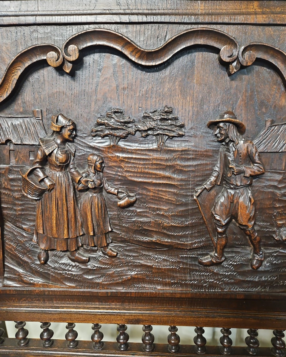 A pair of dark carved oak Breton armchairs featuring backrest panels with relief scenes of folk figures and turned spindle galleries. View VIII