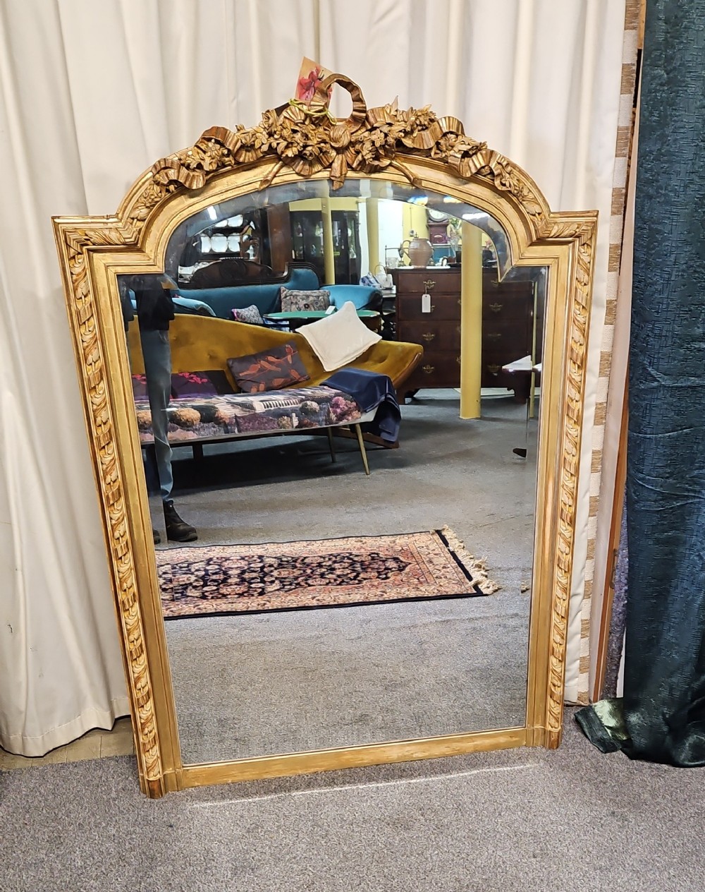 An antique French Louis XVI style giltwood mirror with an arched top, floral garland moulding, and ribbon cresting.
