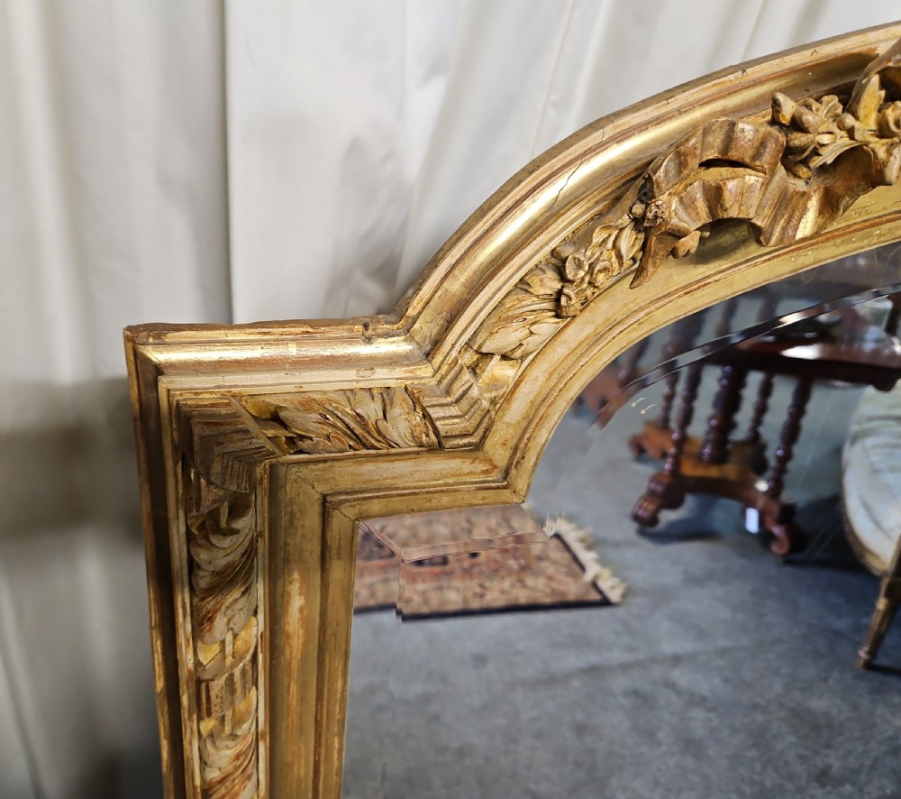 An antique French Louis XVI style giltwood mirror with an arched top, floral garland moulding, and ribbon cresting. View III